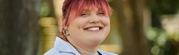 A smiling woman with pink hair relaxes outdoors. — Stock Photo