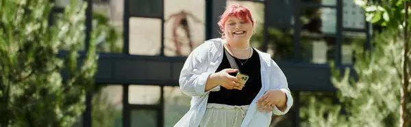 Una donna con i capelli rosa che indossa una giacca bianca sorride alla fotocamera mentre tiene in mano un telefono. — Foto stock