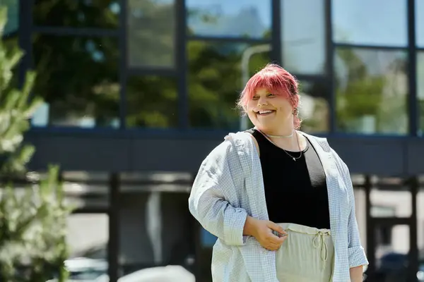 Plus-size woman with pink hair smiles away from the camera, outside a building with large windows — Stock Photo