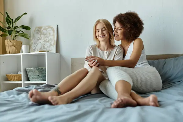 Ein lesbisches Paar in kuscheligen Pyjamas umarmt sich zärtlich auf ihrem Bett. Ihr Lächeln und ihre Nähe strahlen Wärme und Liebe aus. — Stockfoto