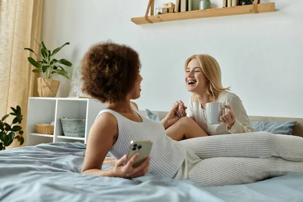 A multicultural lesbian couple enjoys a cozy morning together, laughing and sharing a quiet moment. — Stock Photo