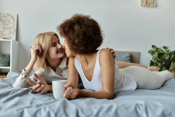 A multicultural lesbian couple relaxes in bed, sharing a cozy moment together. — Stock Photo