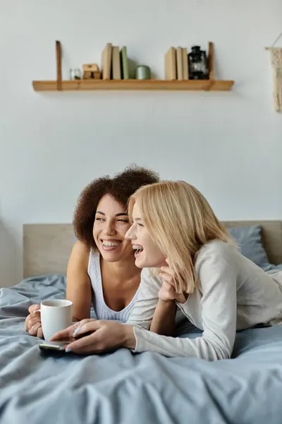 Una coppia lesbica multiculturale ride insieme mentre si rilassa a letto. — Foto stock