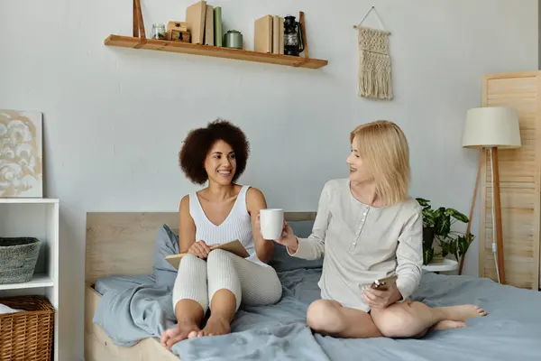 A lesbian couple relaxes on a bed at home, sharing a cup of coffee and a moment of intimacy. — Stock Photo