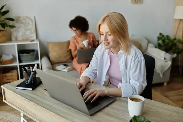 A lesbian couple enjoys a coffee break while working from home, focusing on their respective laptops. — Stock Photo