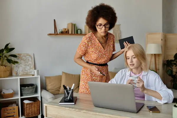 Two women working from home, one pointing at a laptop screen while the other holds a cup of coffee. — Stock Photo