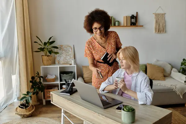 A lesbian couple works from home on a laptop, one woman stands behind the other, smiling and looking at the screen. — Stock Photo