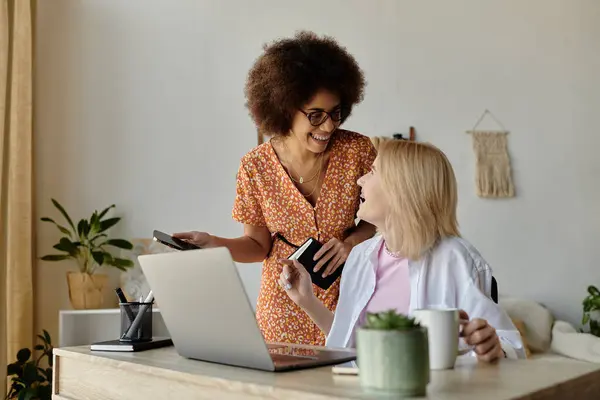 Two women laugh and share a moment while working remotely at home. — Stock Photo