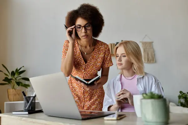 A multicultural lesbian couple works together on a laptop in a home office. — Stock Photo