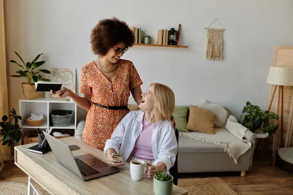 Zwei Frauen lachen und arbeiten gemeinsam an einem Schreibtisch im Wohnzimmer. — Stockfoto