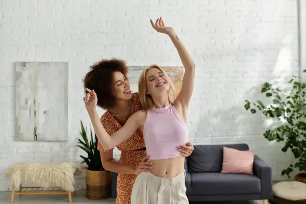 Una pareja lésbica multicultural ríe y baila juntos en su apartamento luminoso y moderno. — Stock Photo