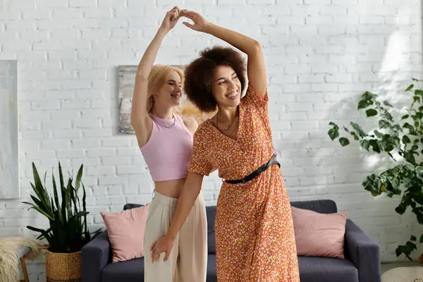 A multicultural lesbian couple dances together in their modern apartment, radiating joy and love. — Stock Photo