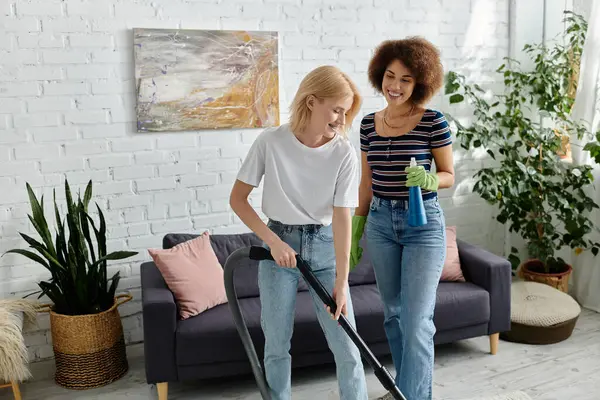Duas mulheres aspiram e limpam seu apartamento moderno juntas, rindo e aproveitando seu tempo. — Fotografia de Stock