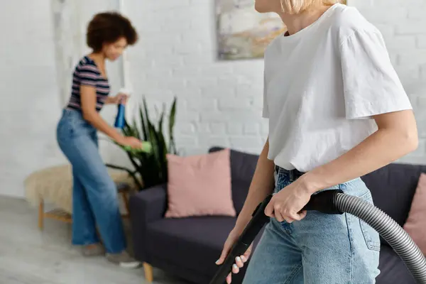 Um casal lésbico limpa seu apartamento moderno juntos, um aspirando e o outro limpando superfícies. — Fotografia de Stock