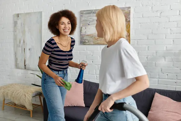 Duas mulheres, um casal lésbico multicultural, alegremente limpar seu apartamento moderno juntos. — Fotografia de Stock