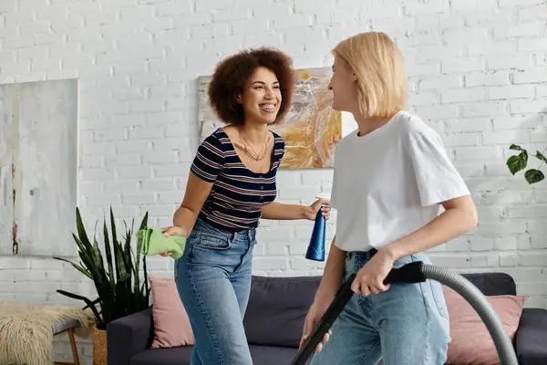 Um casal lésbico ri juntos enquanto limpa seu apartamento moderno. — Fotografia de Stock
