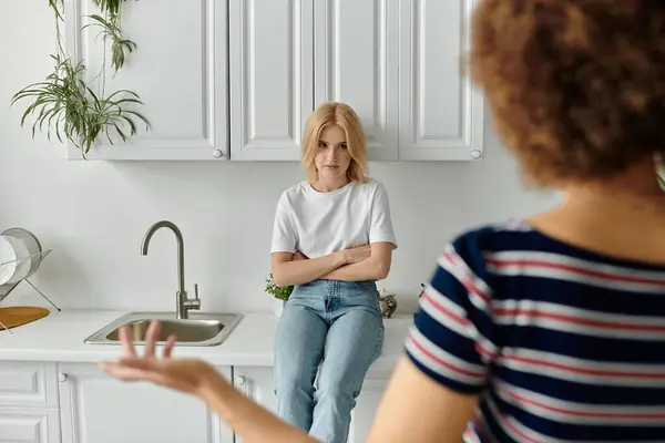 Deux femmes se tiennent dans une cuisine, l'une les bras croisés, l'autre gestuelle d'une expression mécontente. — Photo de stock