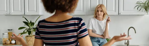 Deux femmes se disputent dans une cuisine, l'une le dos tourné, les mains gestuelles, l'autre assise, regardant ailleurs. — Photo de stock