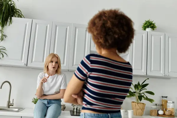 Couple lesbien multiculturel dans la cuisine se disputant. Femme au premier plan bras croisés, femme au comptoir parlant avec expression mécontente — Photo de stock