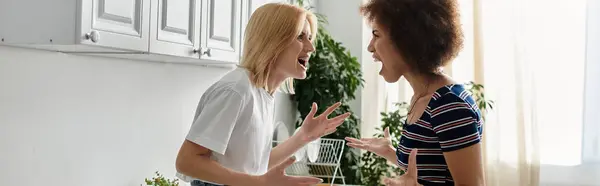 Deux femmes se disputent dans une cuisine, les visages tordus de colère, soulignant un moment tendu dans leur relation. — Photo de stock