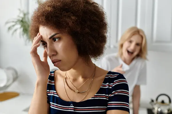 Une femme aux cheveux bouclés en chemise rayée semble malheureuse alors qu'elle écoute son partenaire crier en arrière-plan — Photo de stock