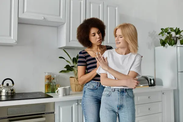 Deux femmes se tiennent dans une cuisine, l'une avec les bras croisés et une expression mécontente, l'autre parlant avec un regard inquiet sur son visage. — Photo de stock