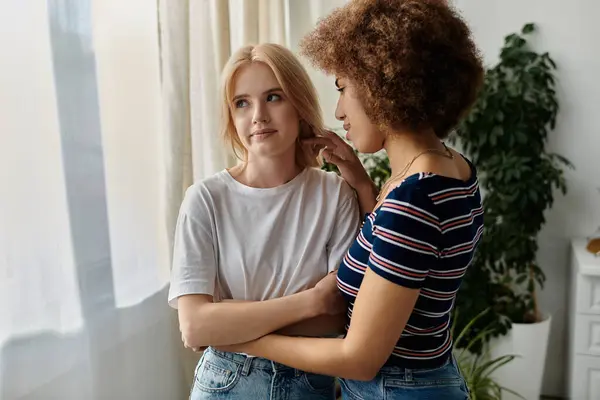 Deux femmes, une blonde et une avec les cheveux bouclés foncés, se tiennent dans une cuisine près d'une fenêtre, regardant malheureux, peut-être argumenter — Photo de stock