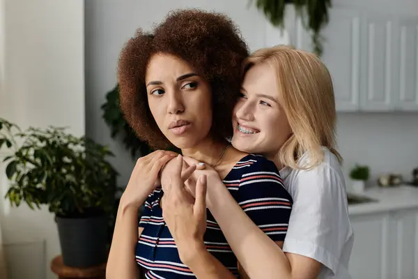 Deux femmes se tiennent dans une cuisine, l'une avec les bras autour de l'autre, tandis que la femme embrassée regarde loin — Photo de stock