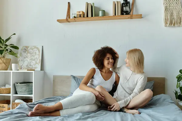 A lesbian couple relaxes on their bed, dressed in cozy home wear, laughing and enjoying each others company. — Stock Photo
