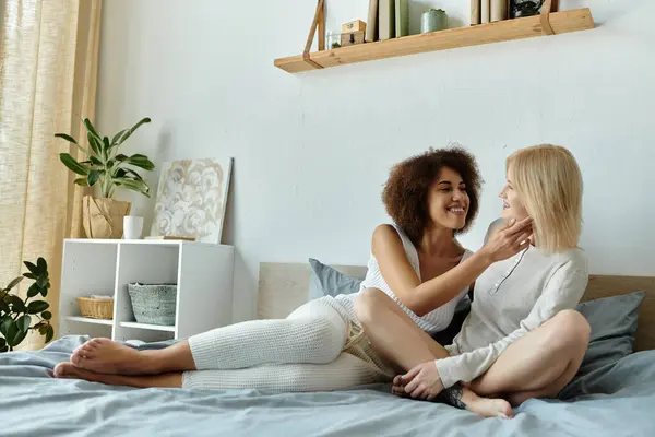 A multicultural lesbian couple cuddles and laughs in a bedroom, enjoying their time together. — Stock Photo