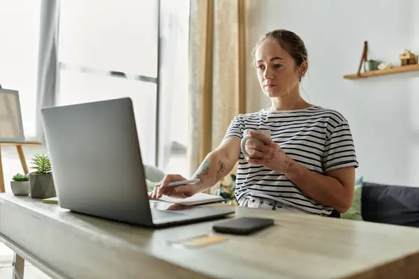 A woman with vitiligo sips her drink while focused on her laptop. — Stock Photo