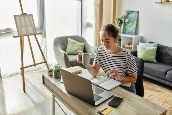 Smiling woman with vitiligo sips coffee while writing in a notebook at home. — Stock Photo