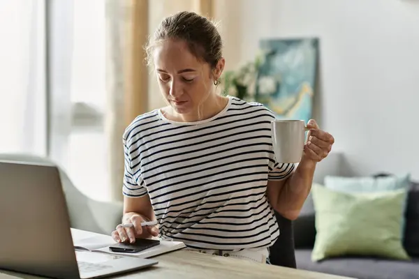 Una giovane donna sorseggia caffè mentre si concentra sul suo computer portatile a casa. — Foto stock