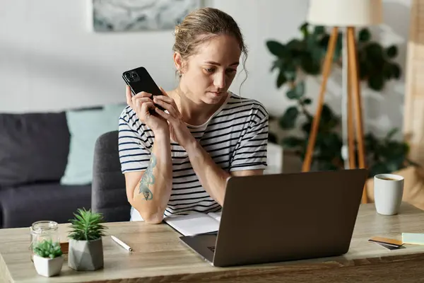 A young woman reflects while using her phone at a wooden desk. — Stock Photo