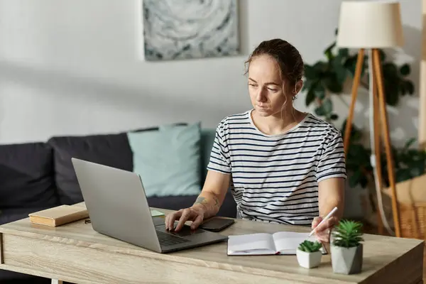 A beautiful woman with vitiligo writes in her notebook while focused on her laptop. — Stock Photo