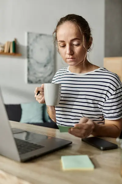 Una mujer pensativa con vitiligo disfruta de su café mientras reflexiona en su escritorio. - foto de stock