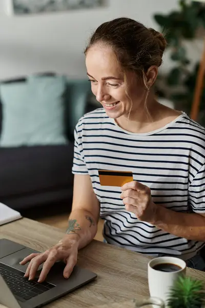 A woman with vitiligo smiles while shopping online with a credit card. — Stock Photo