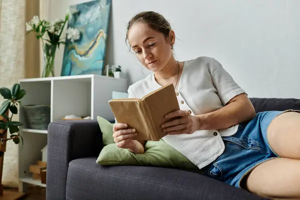 A woman with vitiligo enjoys reading a book on her plush couch. — Stock Photo