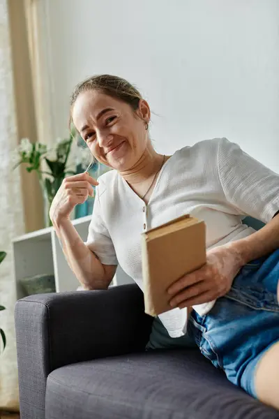 A joyful woman with vitiligo smiles contentedly while reading on a cozy couch. — Stock Photo