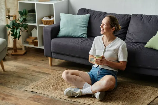 A woman with vitiligo sits happily on the floor, enjoying a warm drink. — Stock Photo