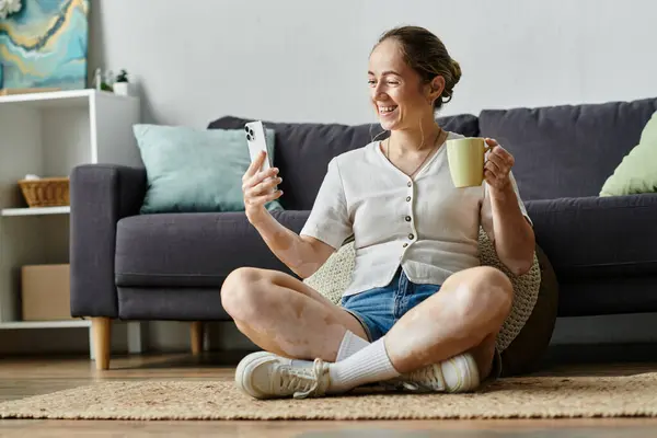 Una mujer sonríe brillantemente mientras charla en su teléfono, bebiendo una bebida caliente. - foto de stock