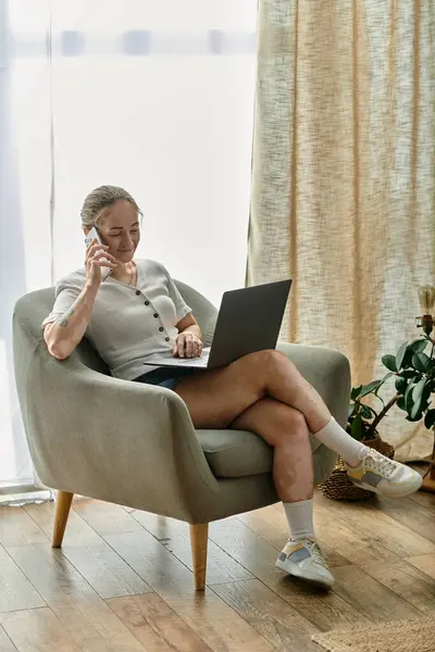 Eine Frau lächelt, während sie mit ihrem Handy telefoniert, bequem mit ihrem Laptop sitzend. — Stockfoto