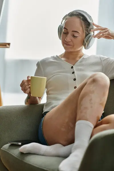 A woman sips tea, relaxed and immersed in her thoughts, wearing cozy headphones. — Stock Photo