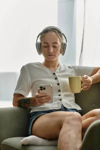 A woman with vitiligo relaxes with tea while listening to music, absorbed in her phone. — Stock Photo