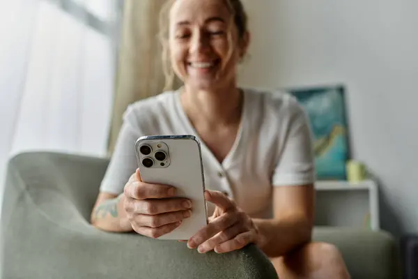 A woman with vitiligo smiles while looking at her phone on a cozy sofa. — Stock Photo