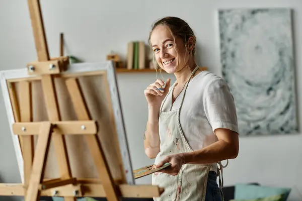 A young woman with vitiligo smiles while painting in her creative workspace. — Stock Photo