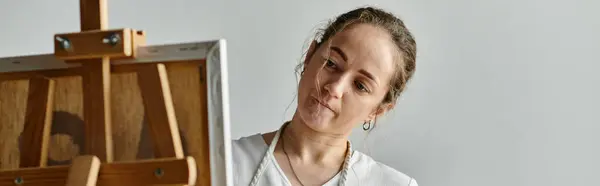 A woman with vitiligo focuses intently on her canvas in a sunlit studio. — Stock Photo