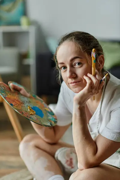 A young artist thoughtfully plans her next vibrant creation while seated in a cozy studio. — Stock Photo