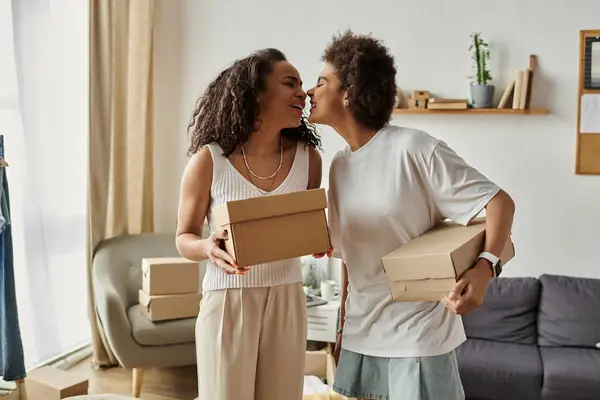 Casal LGBT alegremente upcycling roupas enquanto partilha um momento de concurso, segurando caixas. — Fotografia de Stock