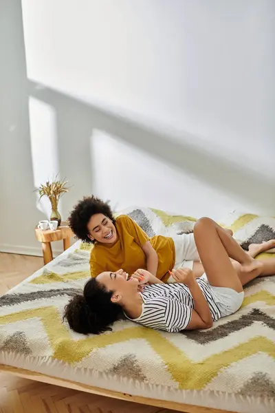 Dos mujeres comparten la risa y el amor en una cama acogedora en su espacio de vida brillante. — Stock Photo